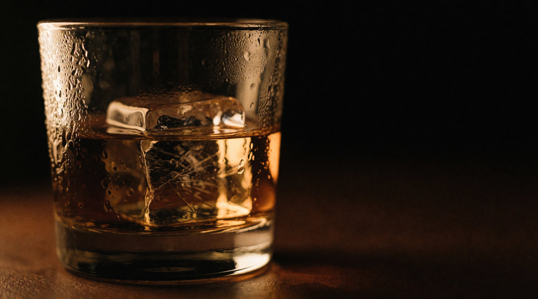 A large clear ice cube in a tumbler of amber whisky.