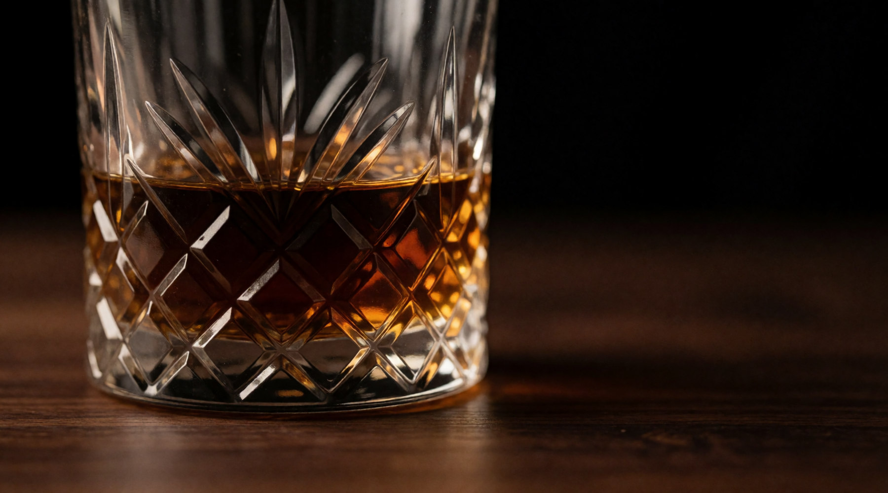 A cut-crystal glass of whisky lit from one side.